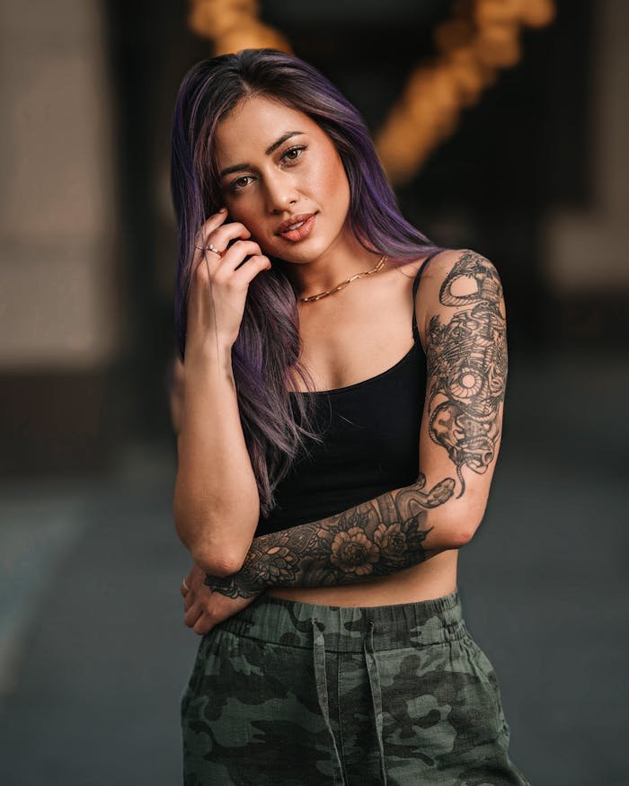 Portrait of a fashionable woman with purple hair and tattoos posing confidently in a trendy outfit.