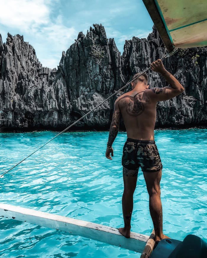 A man stands on a boat enjoying the crystal-clear water and rocky cliffs of El Nido, Philippines.